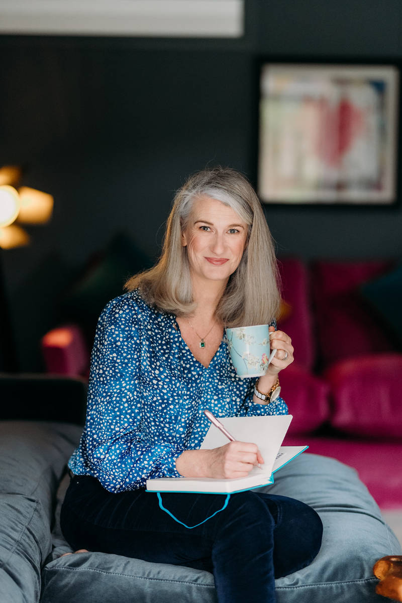 Nicky holding a cup of tea and writing in a journal